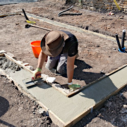 Photo of a handyman trowelling concrete for a greenhouse foundation.