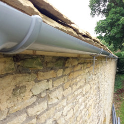 A photo of new plastic guttering with traditional wall brackets on the side of a barn in the Cotswolds