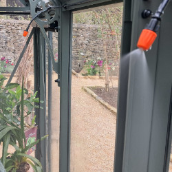 The nozzles of an irrigation system spraying water on plants in a greenhouse